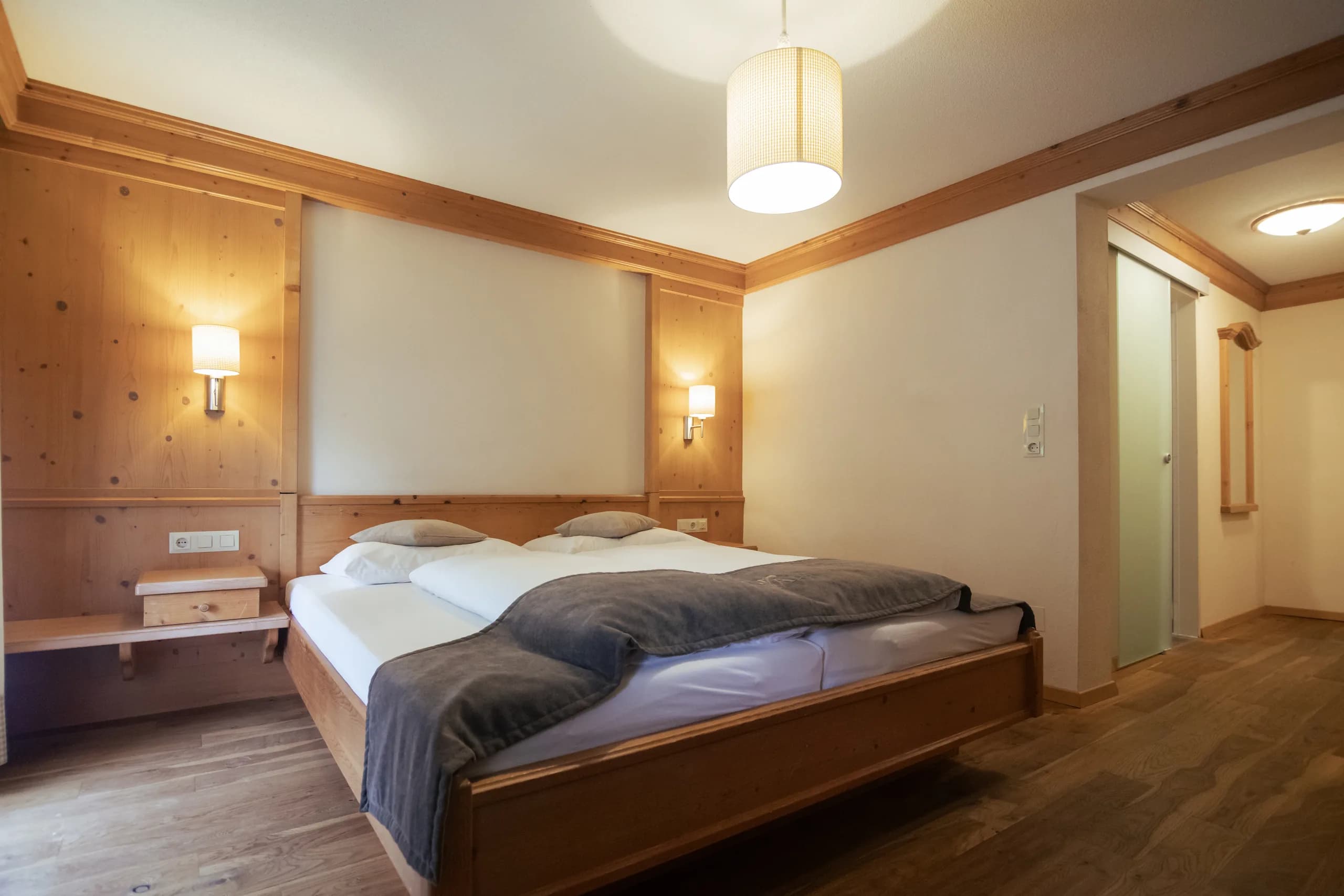 Bett mit dunkelgrauer Decke und stimmungsvoller Pendelleuchte im Natur Raum DZ der Natur Residenz Anger Alm