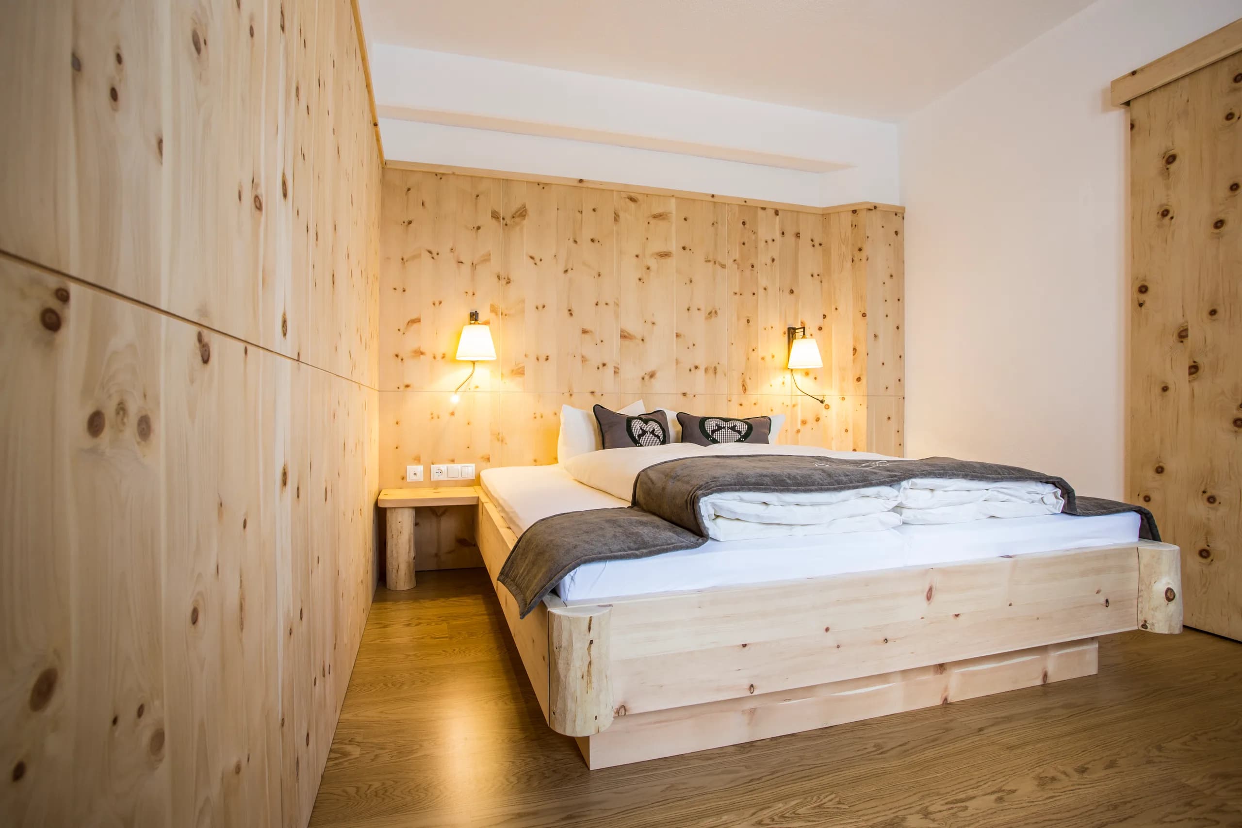 Zirbenholzbett mit Wandleuchten und Nachttisch in der Zirben-Suite der Natur Residenz Anger Alm