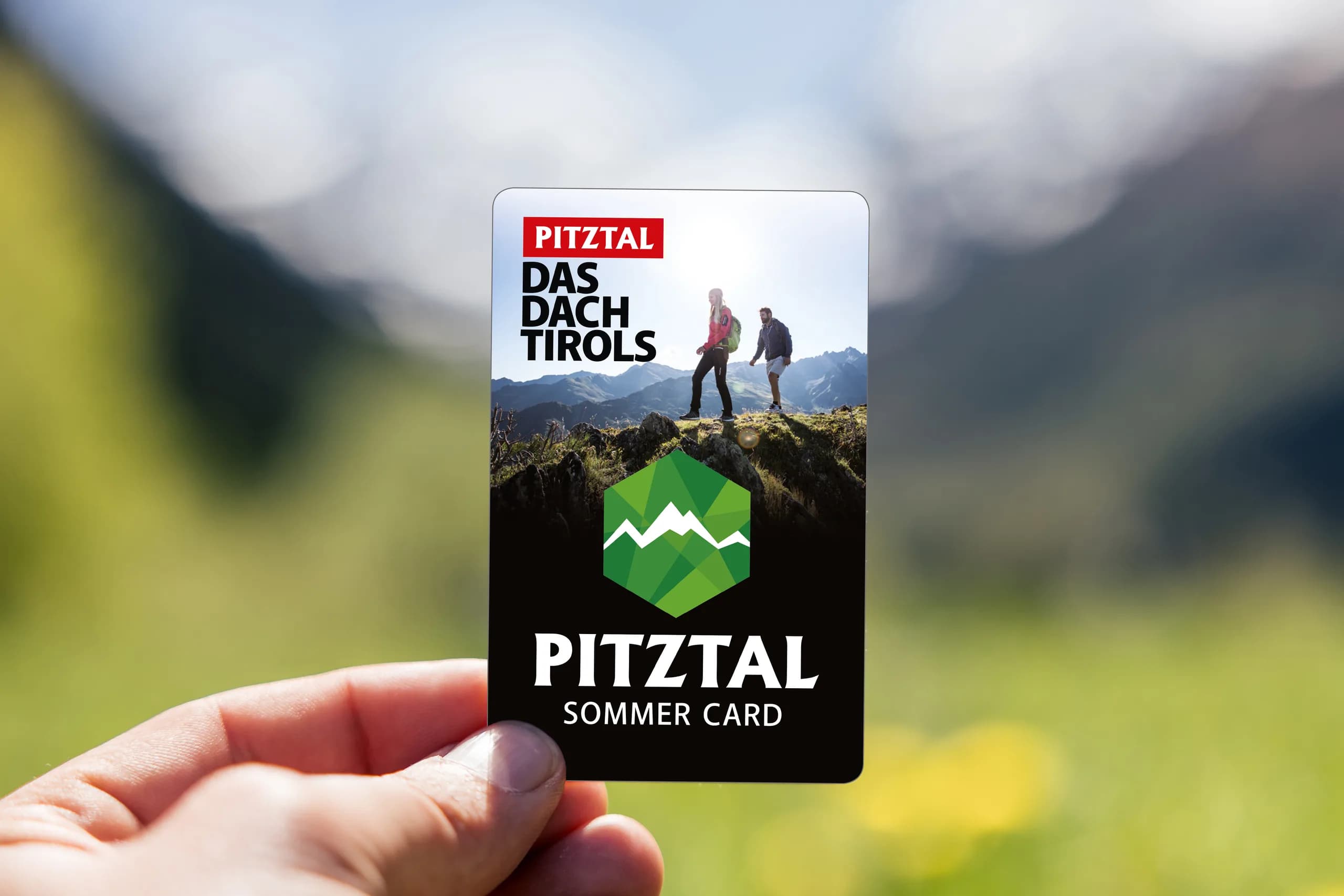 Hand hält die Pitztal Sommer Card vor einer Bergwiese
